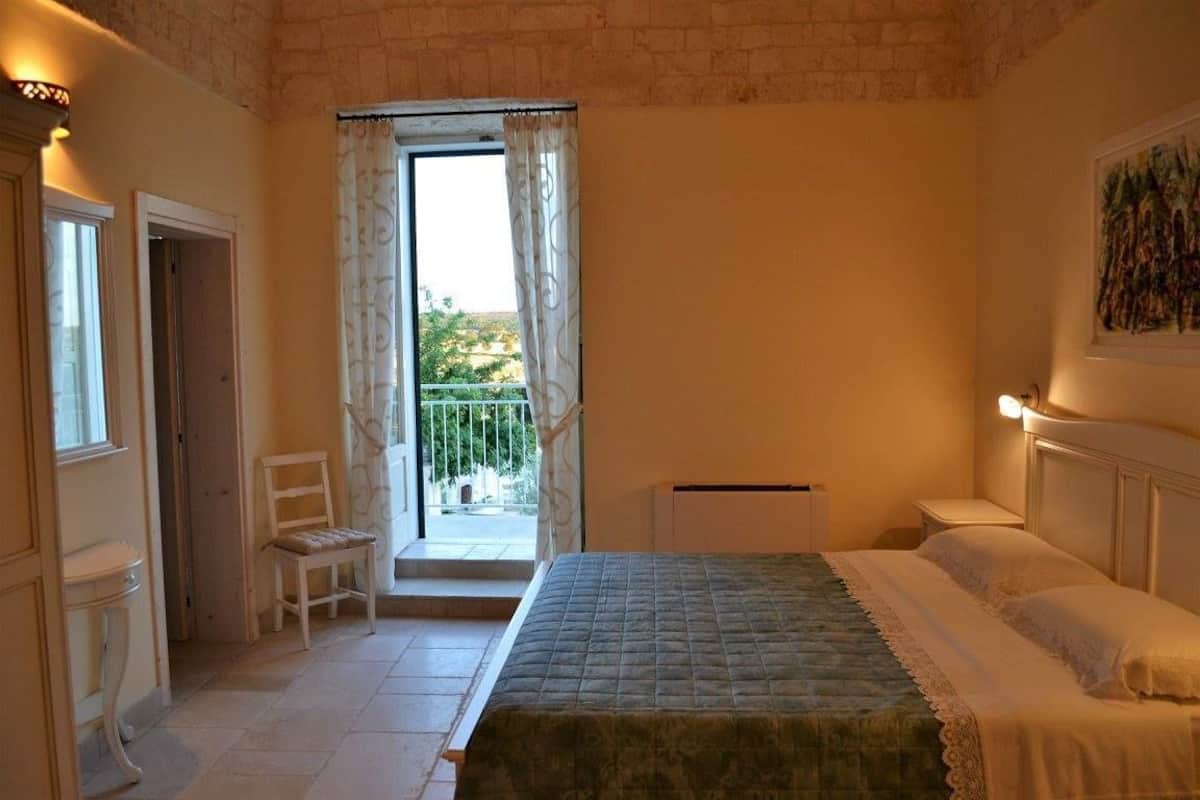 Ein Schlafzimmer mit einem Bett, einem Sessel, einem Nachttisch und einem Fenster mit Vorhängen.
