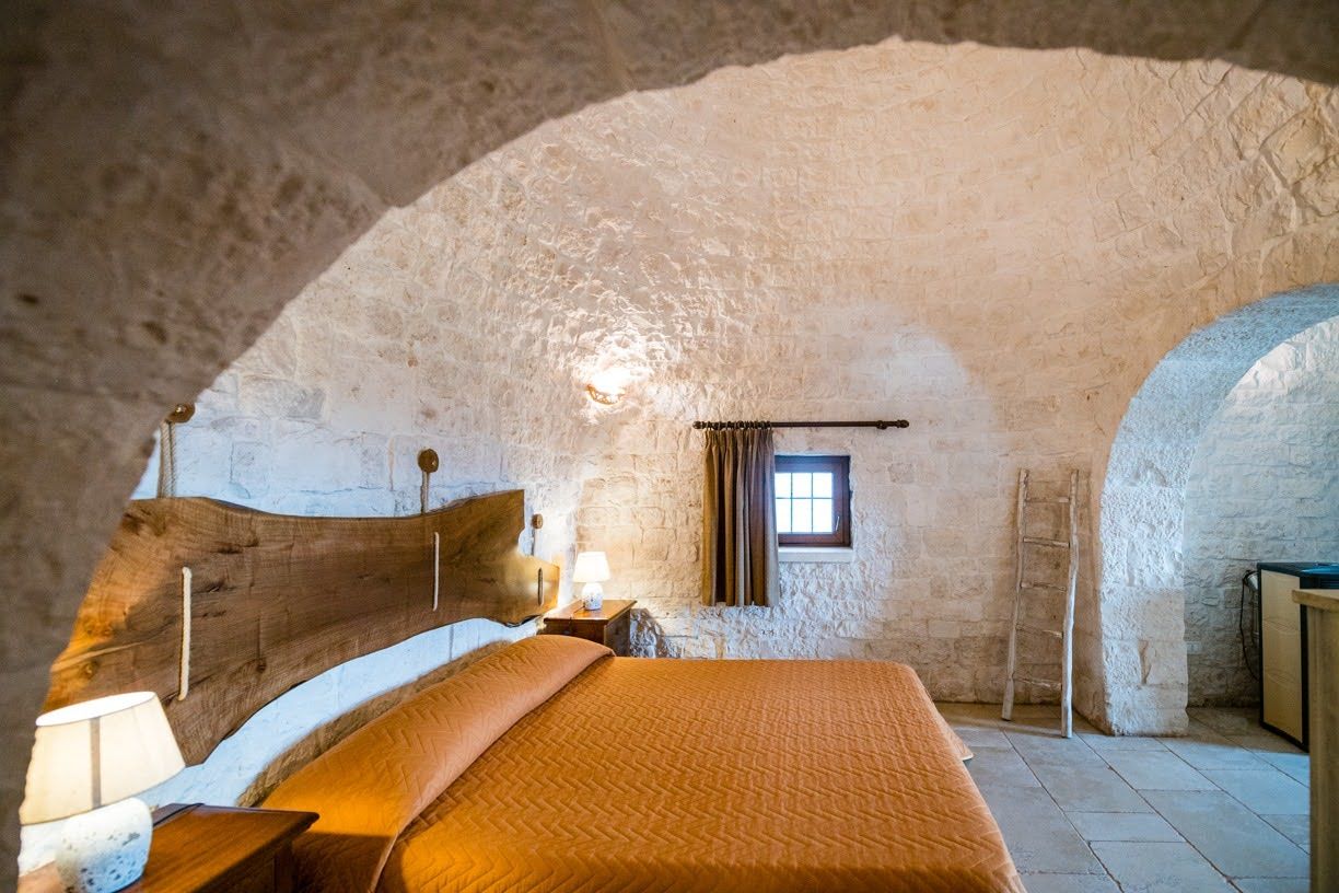 Ein rustikales Schlafzimmer mit einer Steinwand, einem hölzernen Bett, einem Nachttisch, einer Lampe und einem Fenster.