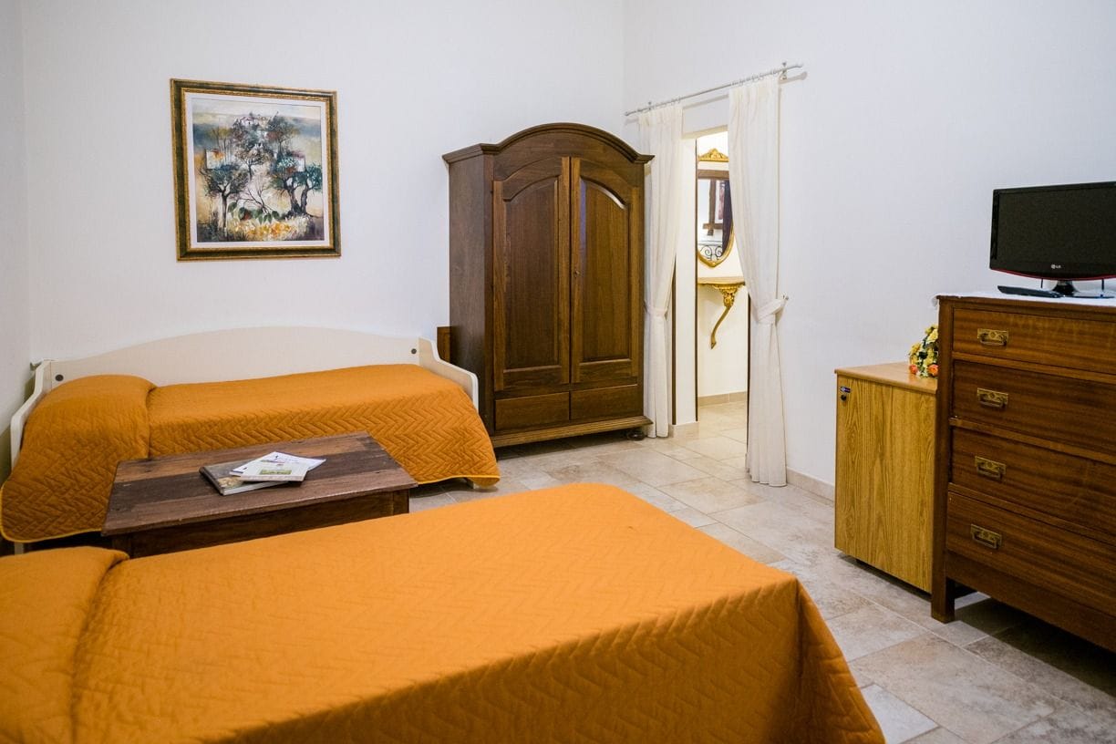 A room with two beds, a wooden wardrobe, a television, and a painting on the wall.