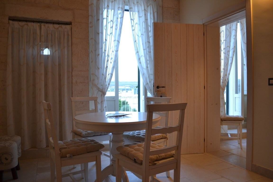 Ein Essbereich mit rundem Tisch und vier Stühlen, ein Fenster mit durchscheinenden Vorhängen und Meerblick.