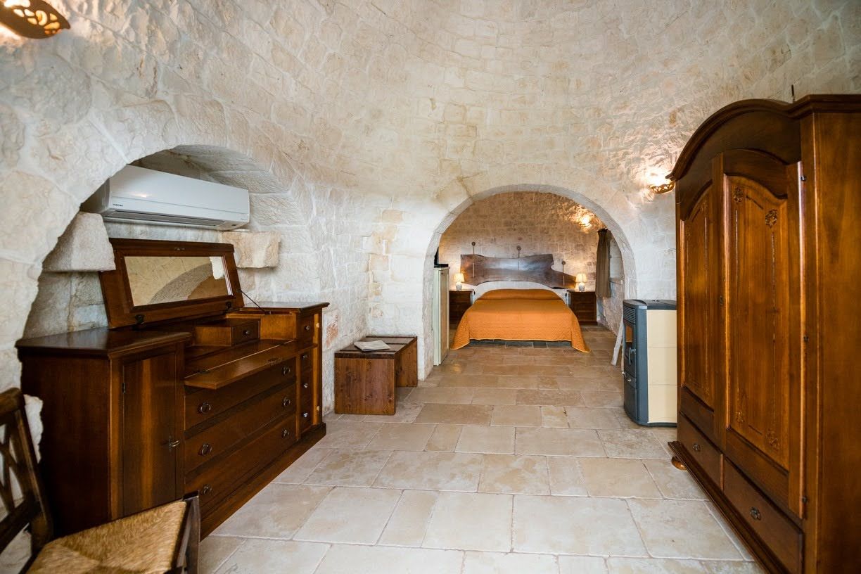 A room with stone walls, a bed with an orange bedspread, wooden furniture, and a vintage air conditioner.