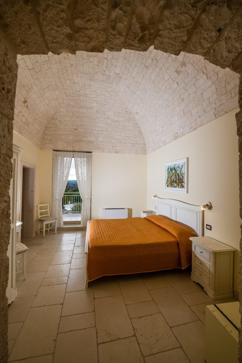 A bedroom with a bed, a chair, a bedside table, and a window with curtains.