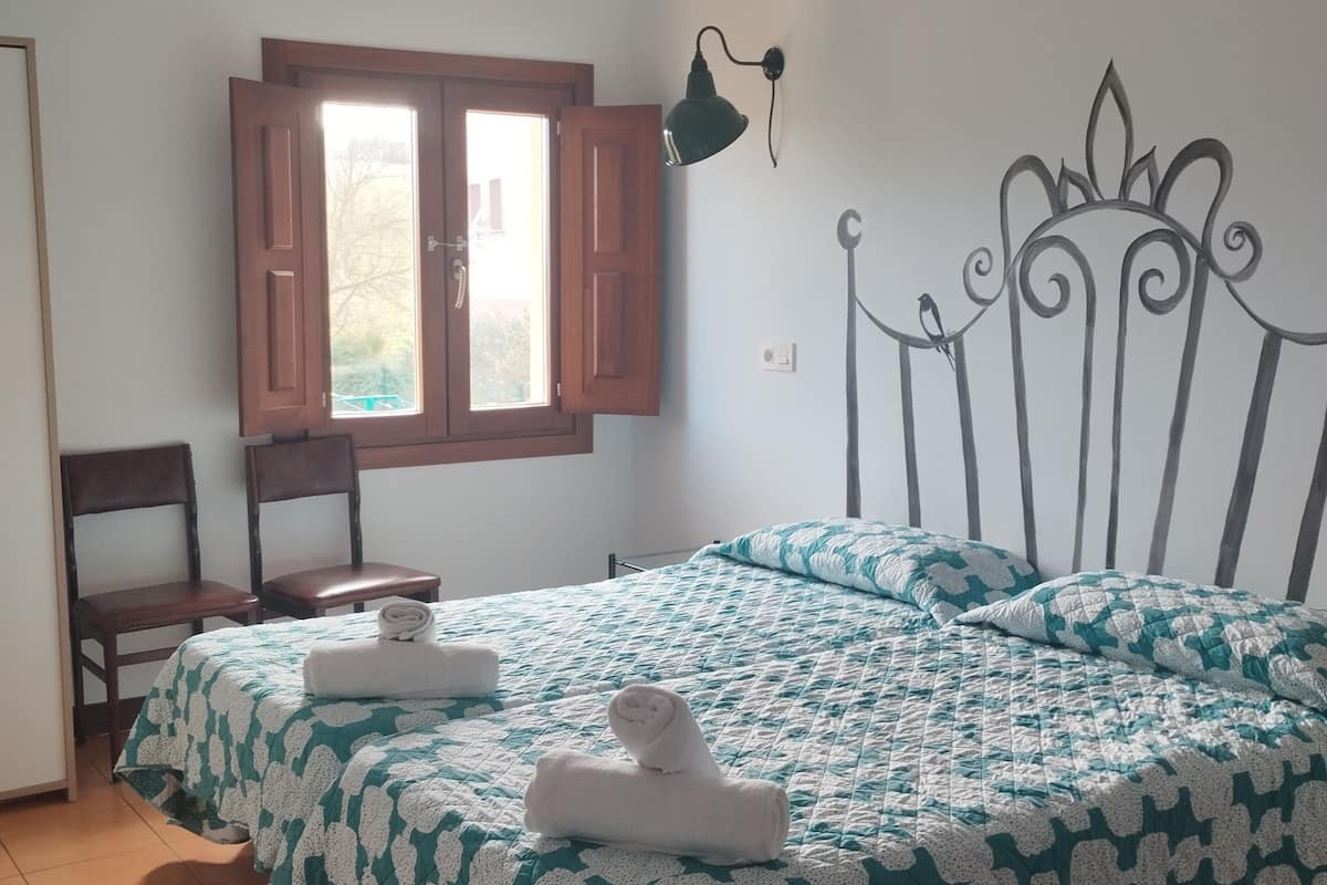 Une chambre à coucher avec un lit, une fenêtre, une chaise et une lampe fixée au mur.