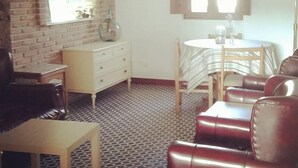 Une pièce avec un mur en briques, une commode blanche, une table ronde avec des chaises et un canapé en cuir.