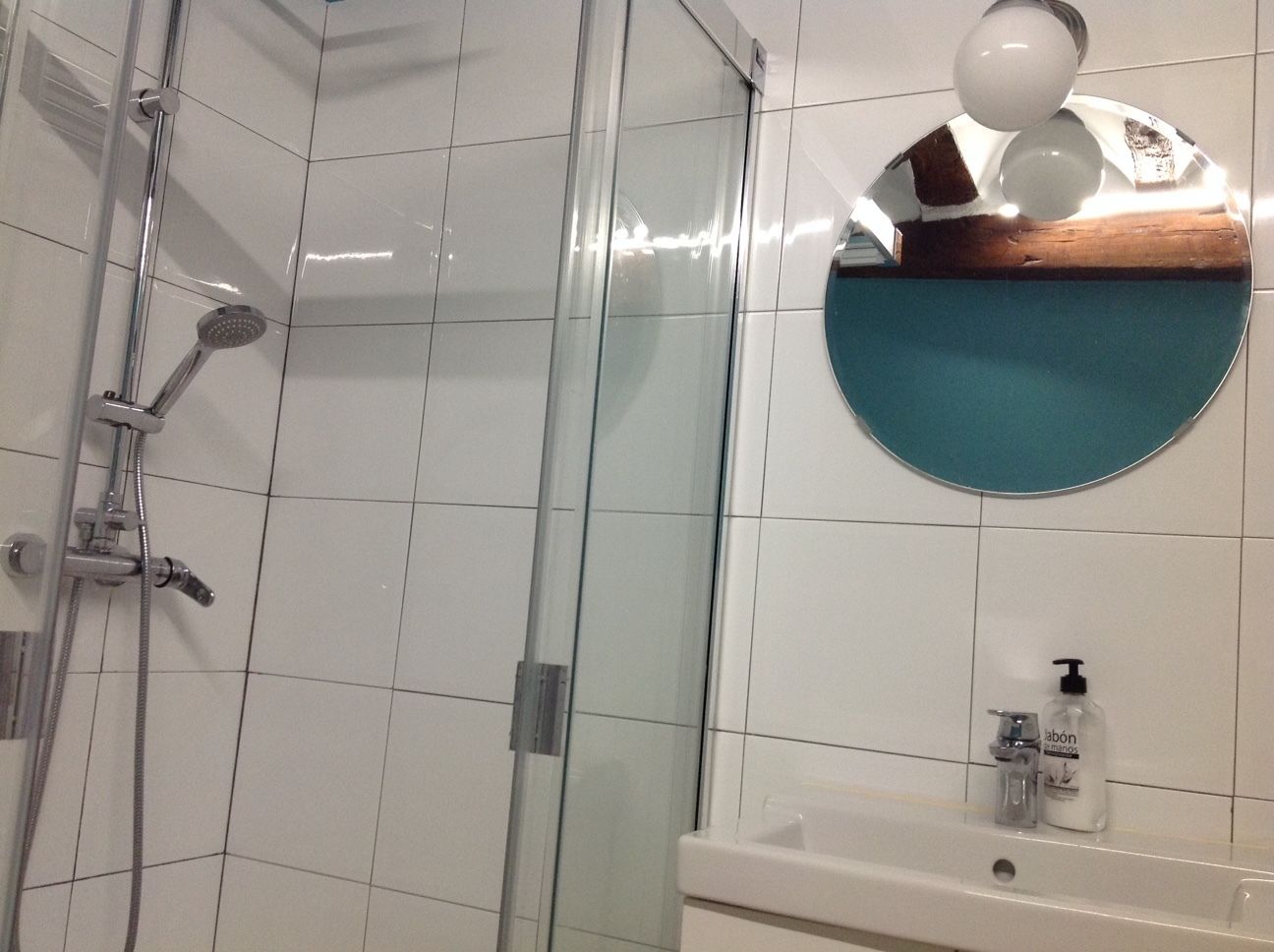 A bathroom with a glass shower enclosure, a white sink with a soap dispenser, and a mirror with a teal frame.