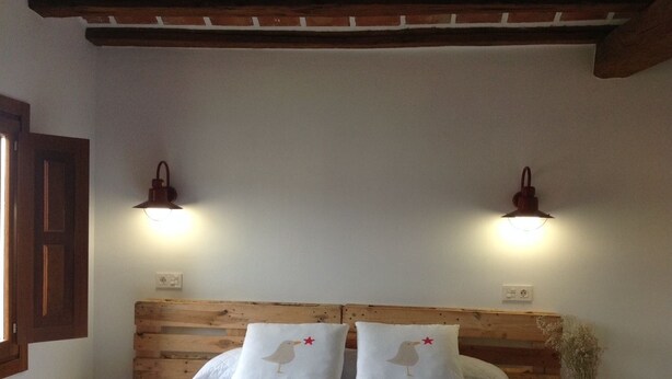 Un lit avec une tête de lit en bois, deux tables de chevet et deux lampes fixées au mur.