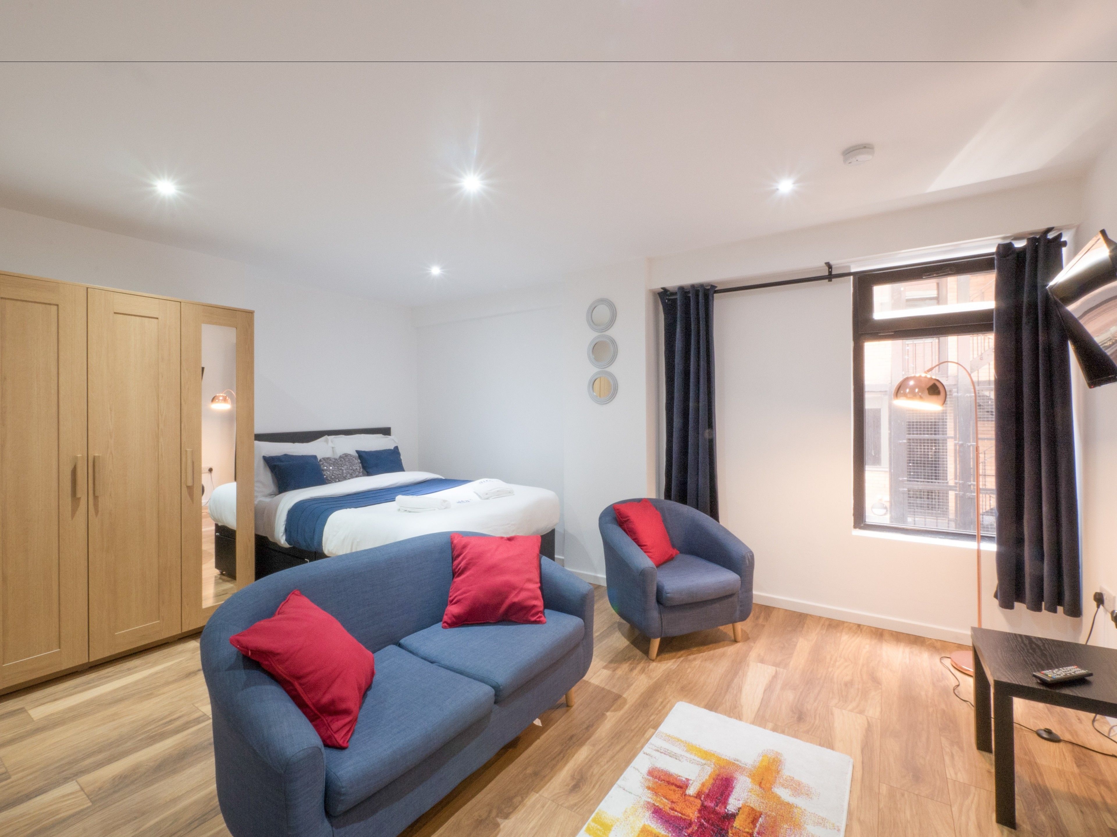 A modern bedroom with a bed, a blue sofa, a chair, a wooden wardrobe, and a window with curtains.