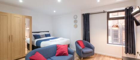 A modern bedroom with a bed, a blue sofa, a chair, a wooden wardrobe, and a window with curtains.