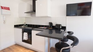 A modern kitchen with white cabinets, a black countertop, a stove, a sink, a toaster, and a chair. - Victoria House Apartments (Leeds)