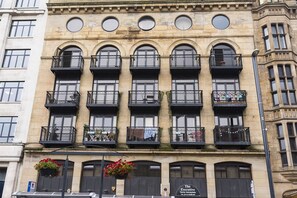 A building with multiple balconies, each with a black railing and potted plants. - Victoria House Apartments (Leeds)