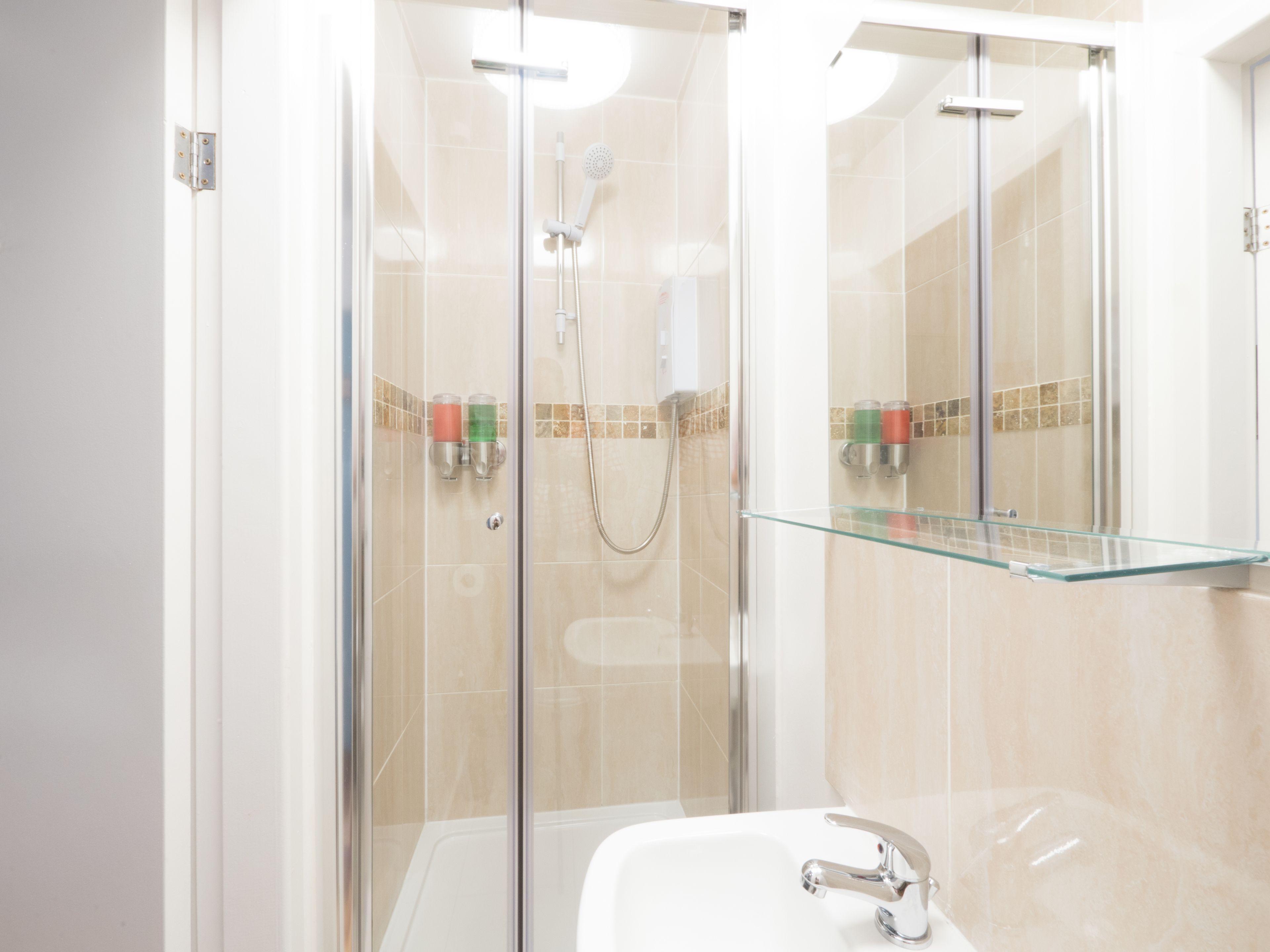 Un baño moderno con cabina de ducha de vidrio, repisa de vidrio sobre el lavabo y un lavabo blanco con grifo cromado.
