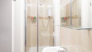 A modern bathroom with a glass shower enclosure, a glass shelf above the sink, and a white sink with a chrome faucet. - Victoria House Apartments (Leeds)