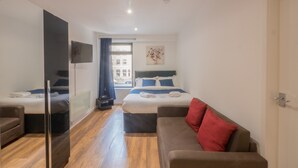 A modern hotel room with two beds, a sofa, a TV, and a window with curtains. - Victoria House Apartments (Leeds)