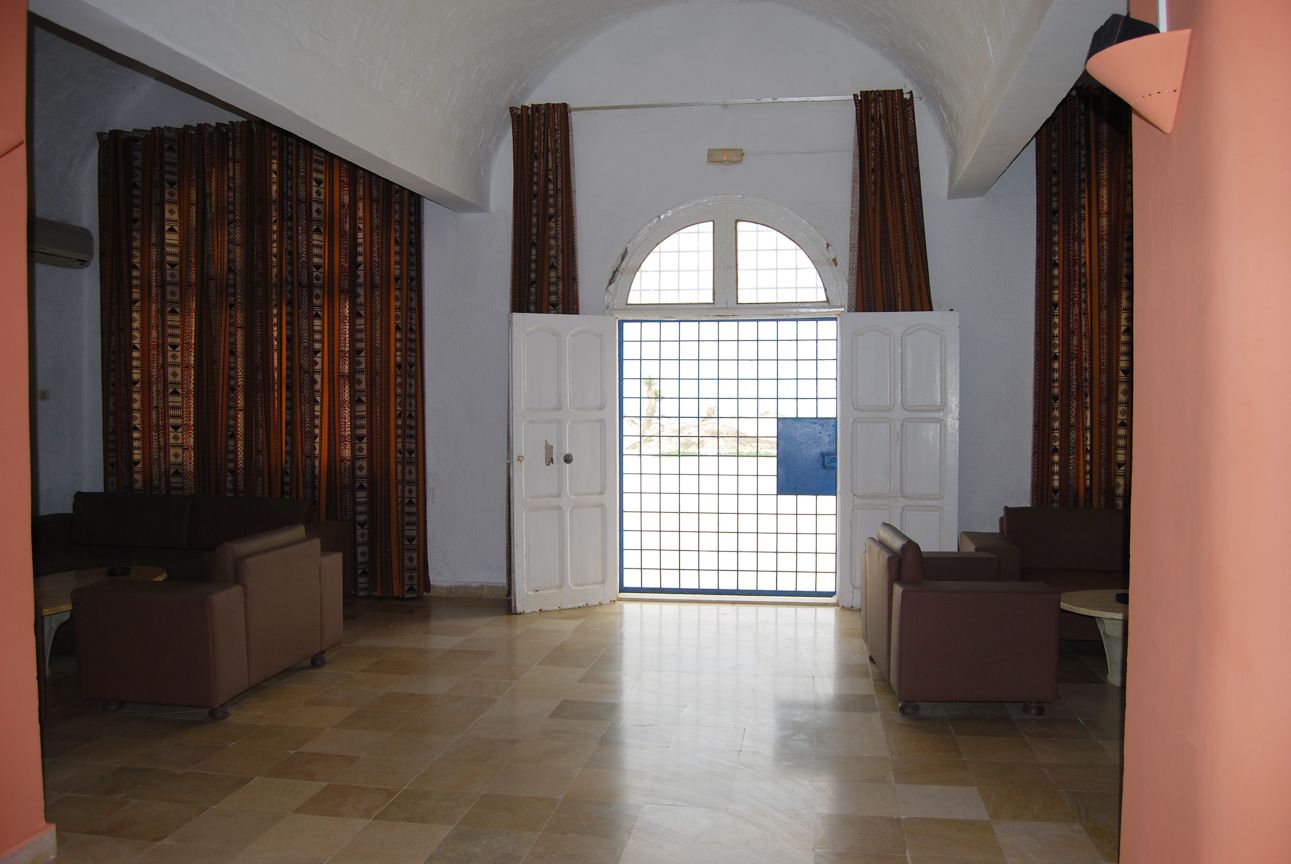 Una habitación amplia con suelo de baldosas, una puerta blanca con diseño de cuadrícula y dos sofás.