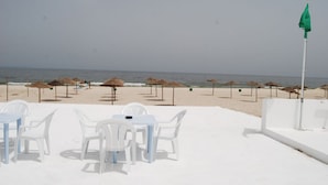 A beachside restaurant with white tables and chairs, thatched umbrellas, and a view of the ocean. - Hôtel El Andalous (Soliman)