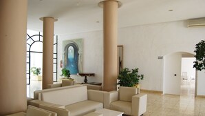 A spacious lobby with beige sofas, large pillars, and a painting of an archway. - Hôtel El Andalous (Soliman)