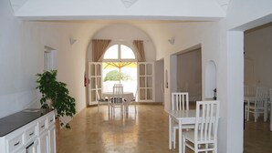 A spacious room with a dining area, white furniture, and a large window with curtains. - Hôtel El Andalous (Soliman)