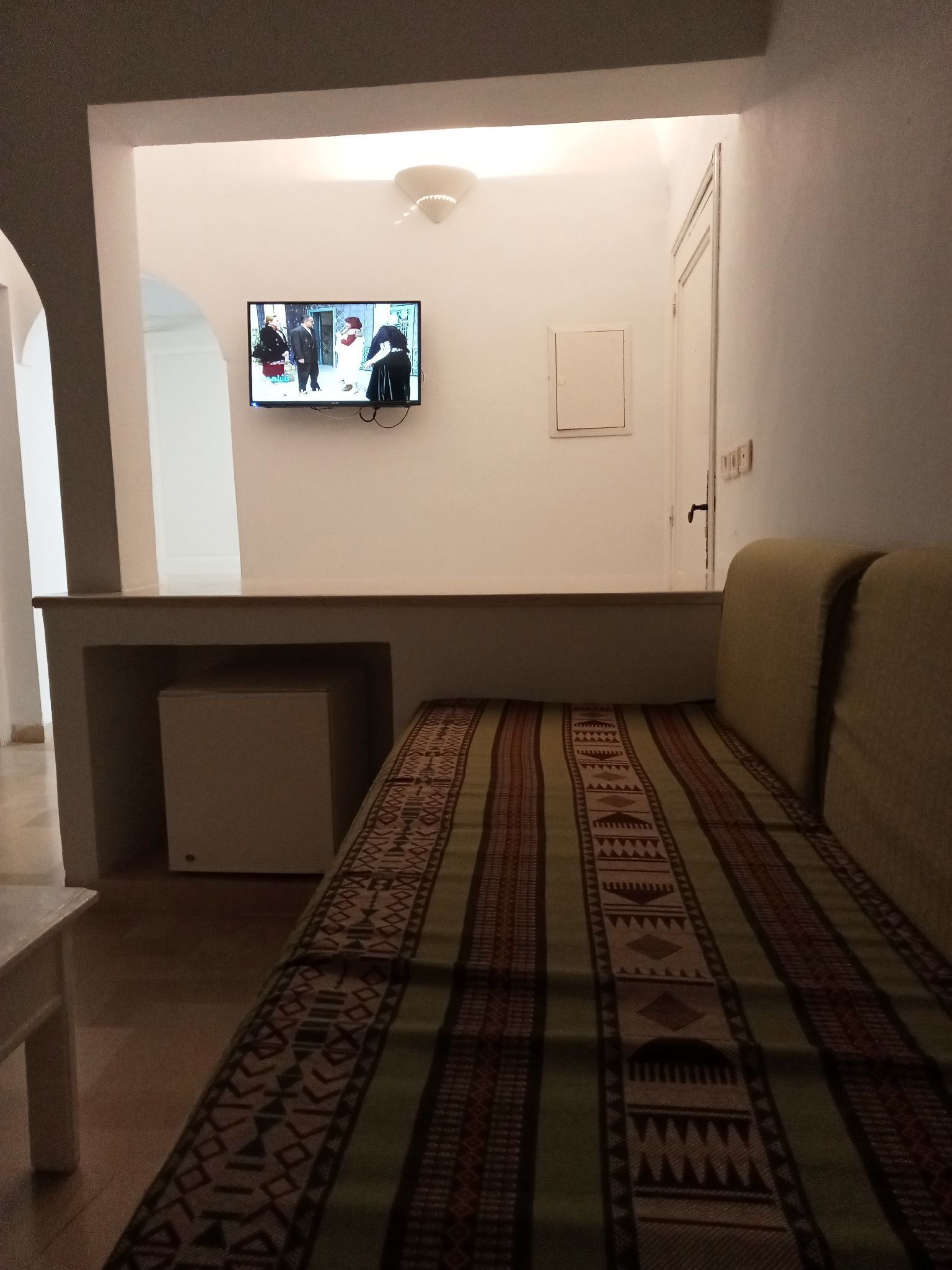Una sala de estar con un televisor montado en la pared, una alfombra estampada y un sofá.