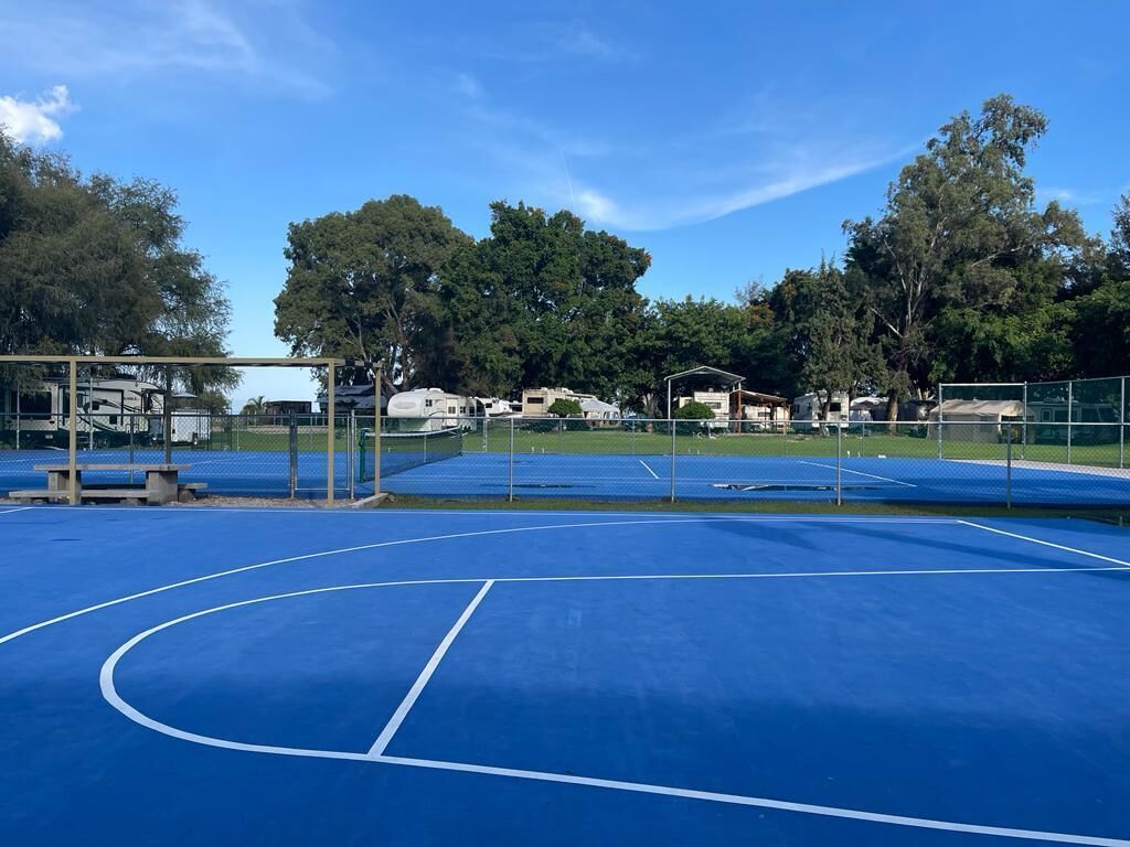 Una cancha de tenis al aire libre con piso azul y líneas blancas delimitadoras.