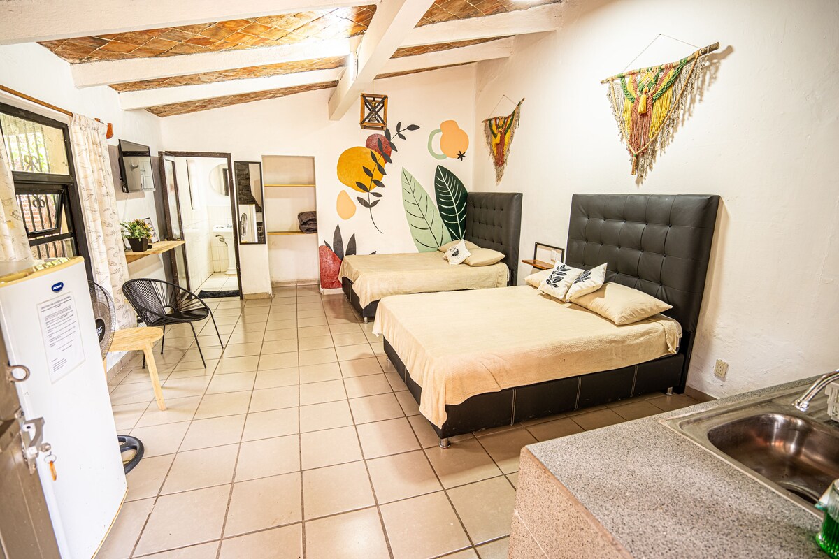 A compact hotel room with two beds, a kitchenette, and a small bathroom.