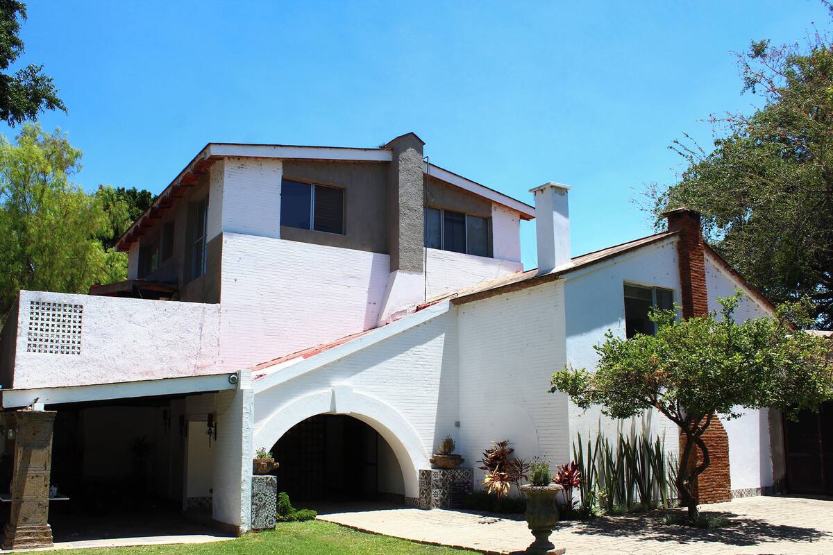A two-story house with a white exterior, a covered driveway, and a small garden with various plants.