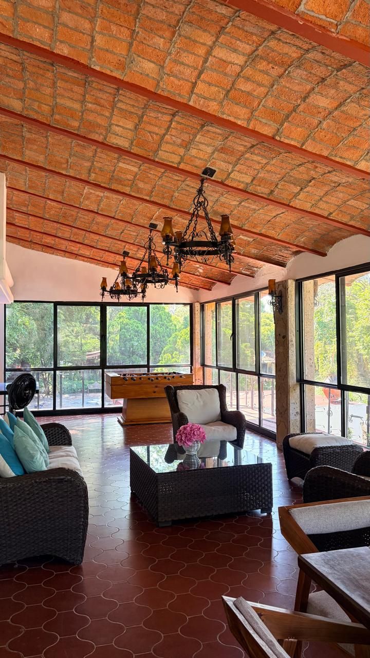 Una habitación amplia con techo alto, ventanas grandes y un área de estar central con sofás y una mesa de centro.
