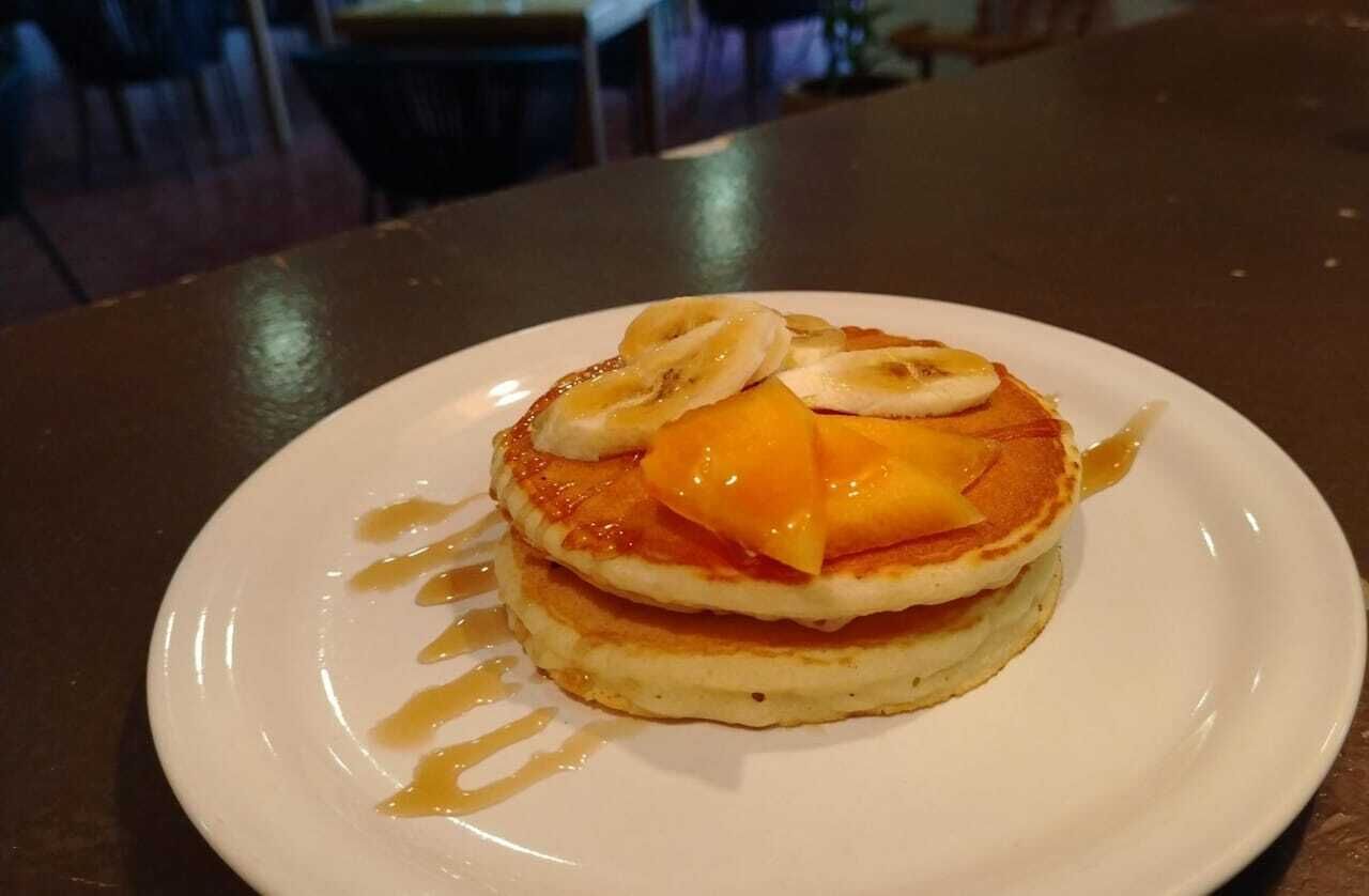 Un plato de panqueques cubiertos con rodajas de plátano y queso derretido, rociados con jarabe.