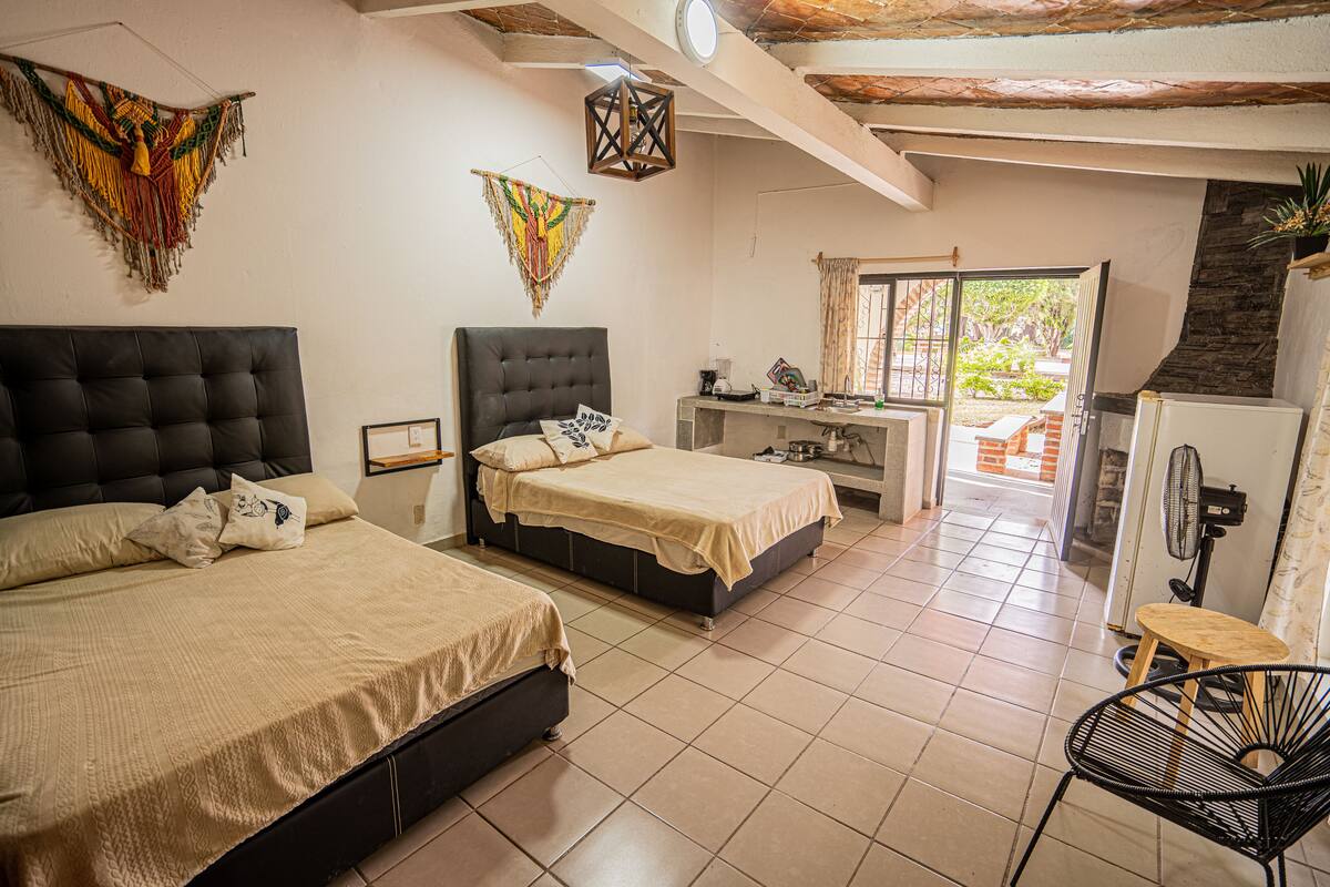 A room with two beds, a desk, a chair, and a fan.