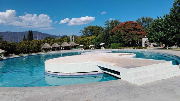 A swimming pool with a circular design, surrounded by a paved area and thatched umbrellas. - Roca Azul (Jocotepec)