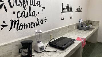 A kitchen with a blender, coffee maker, and a countertop with a kettle and utensils.