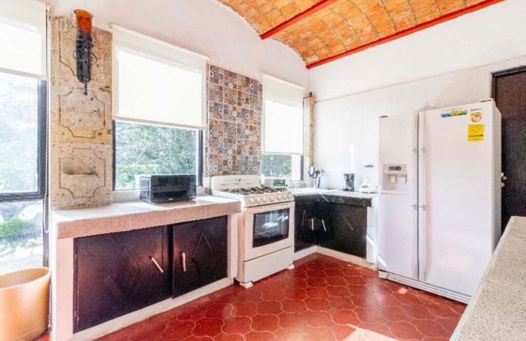 A kitchen with a stove, oven, refrigerator, and a window with a view of greenery.