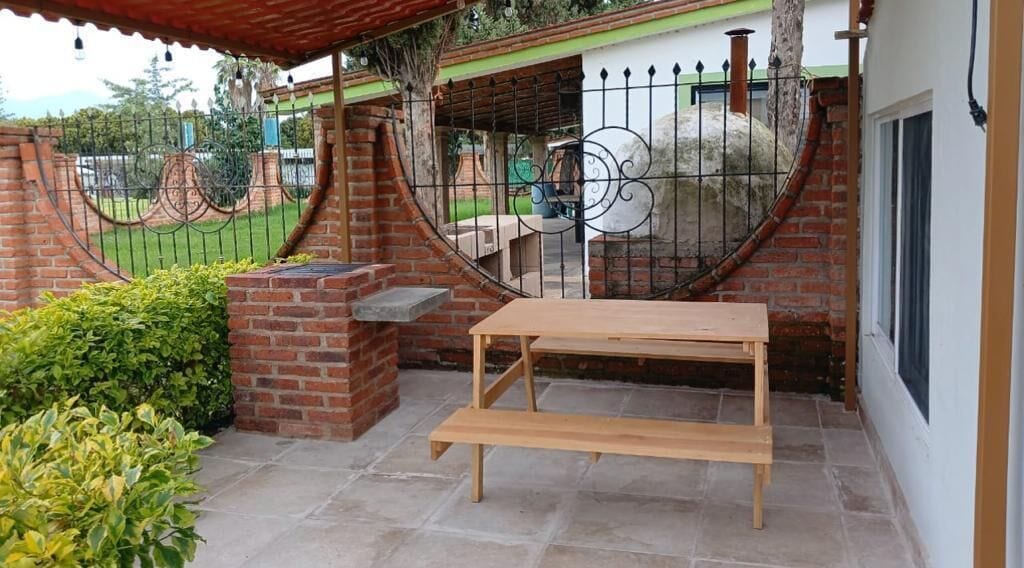 A patio with a wooden table and bench, surrounded by a brick wall and a metal gate.