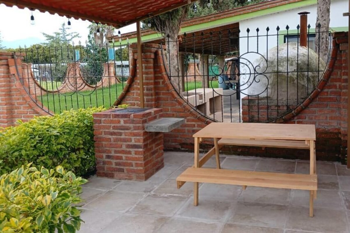 A patio with a wooden table and bench, surrounded by a brick wall and a metal gate.
