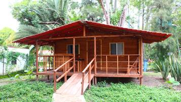 A wooden cabin with a red roof, a wooden deck, and a staircase leading to the entrance.