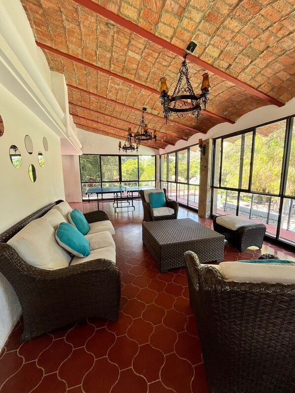 Una habitación amplia con mobiliario de mimbre, ventanas grandes y techo de ladrillo.