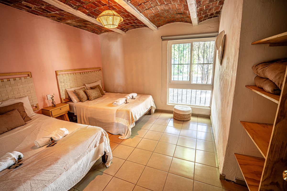 A hotel room with two beds, a window with a view, and a brick ceiling.