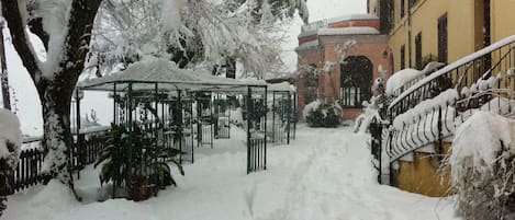 A snow-covered courtyard with a gazebo, a staircase, and a building with a yellow facade.
