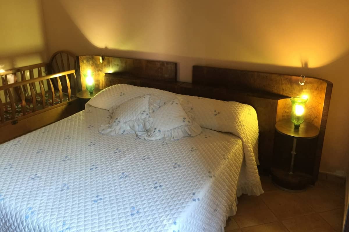 A neatly made bed with a quilted blanket and pillows, a wooden headboard, and two bedside lamps with warm lighting.