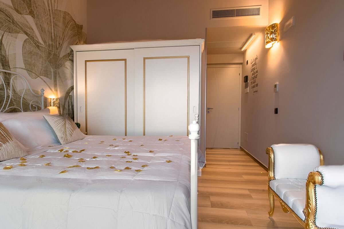 A bedroom with a bed, a nightstand, a wall-mounted lamp, and a door leading to another room.