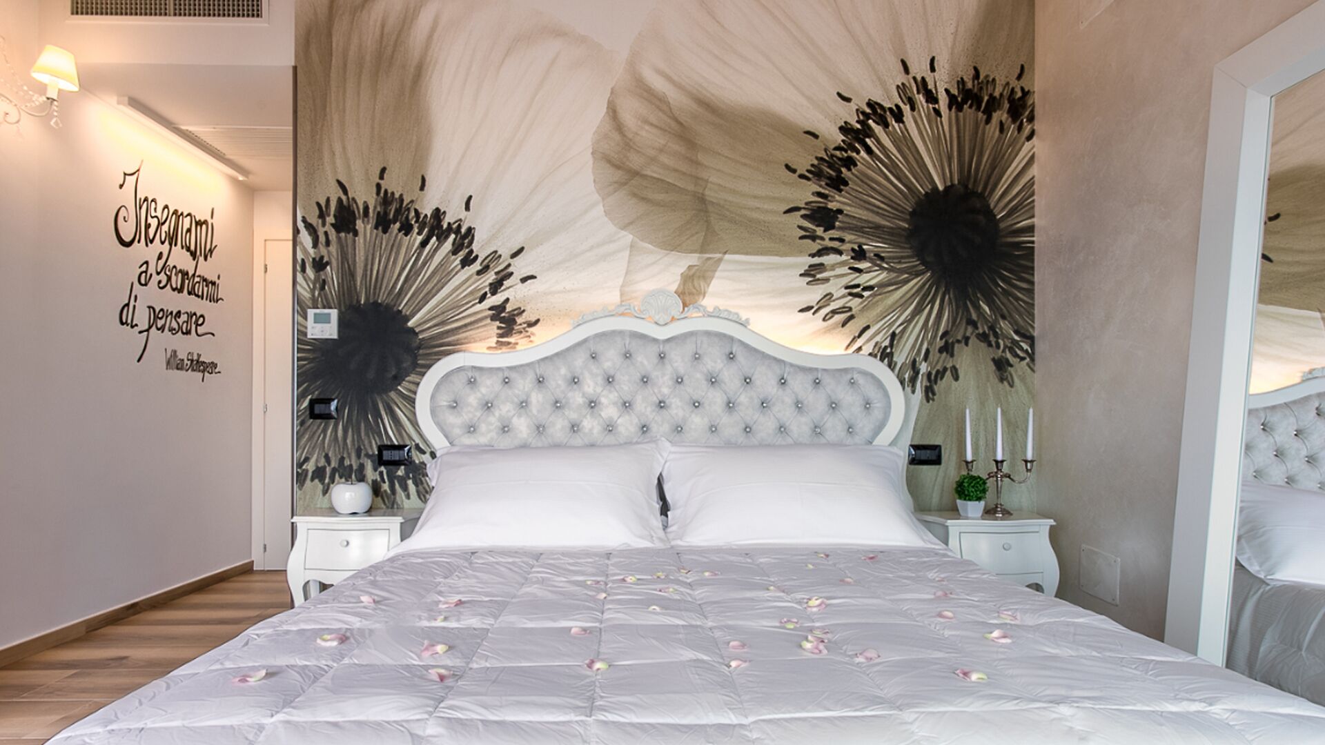 Un dormitorio con cabecera capitonada, cama con edredón blanco y decoración en la pared.