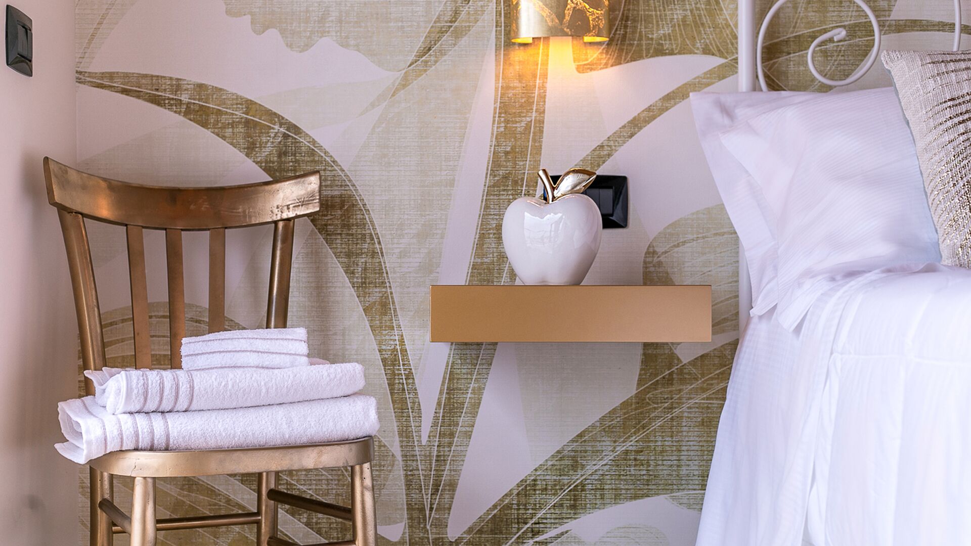 Una habitación de hotel con una silla de madera, una mesita de noche con un florero y una cama con ropa blanca.