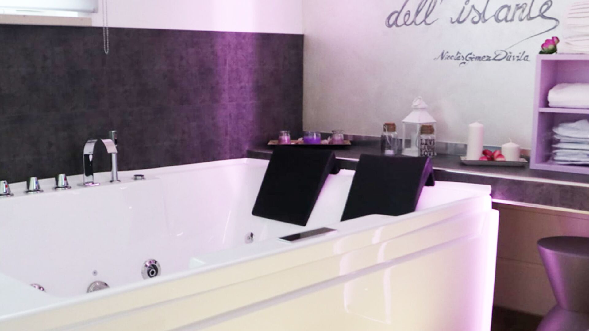 A modern bathroom with a large bathtub, a vanity with a mirror, and a shelf with towels and toiletries.