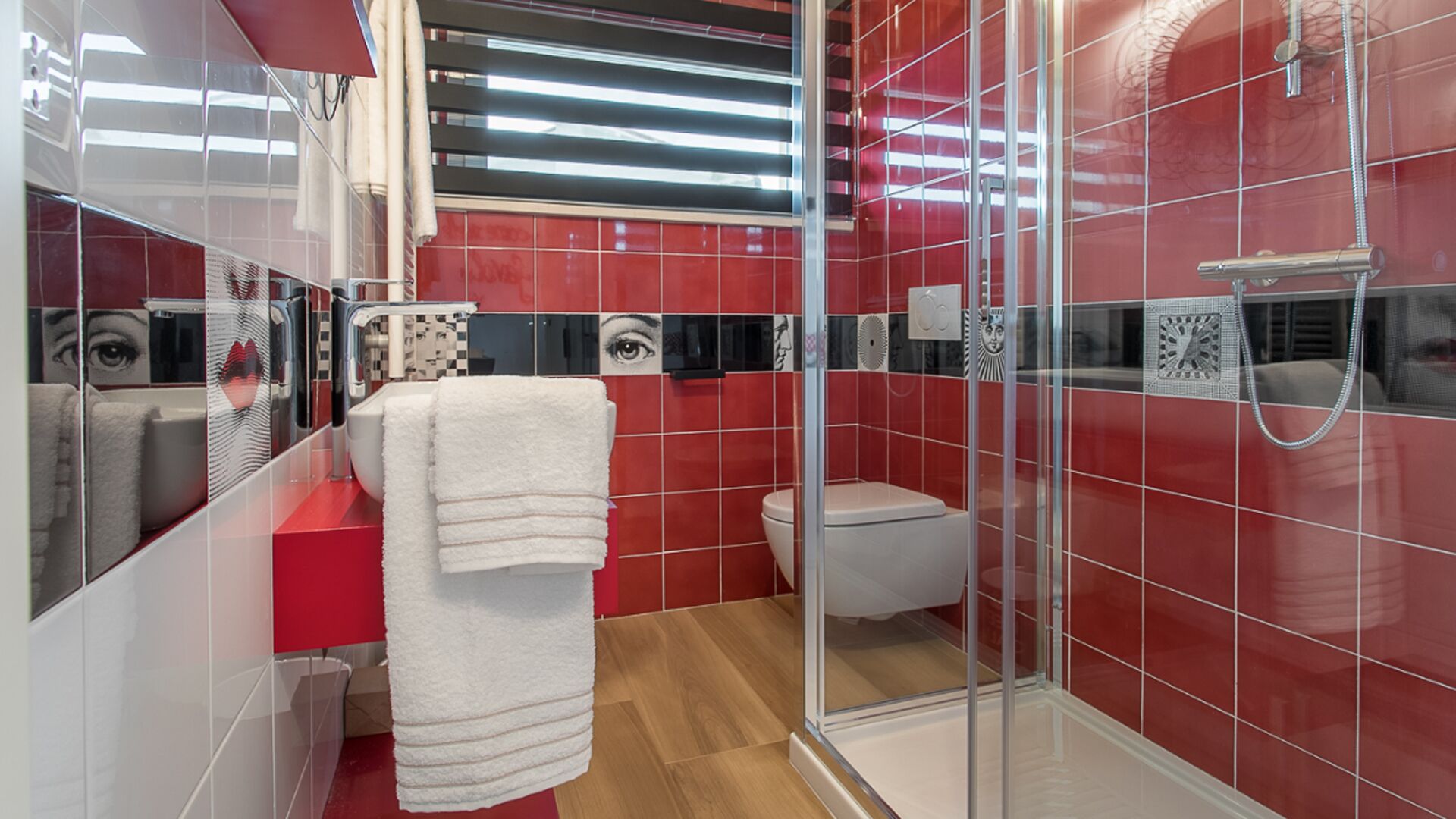 A modern bathroom with red tiles, a glass shower enclosure, and a white sink.