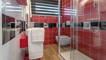 A modern bathroom with red tiles, a glass shower enclosure, and a white sink.