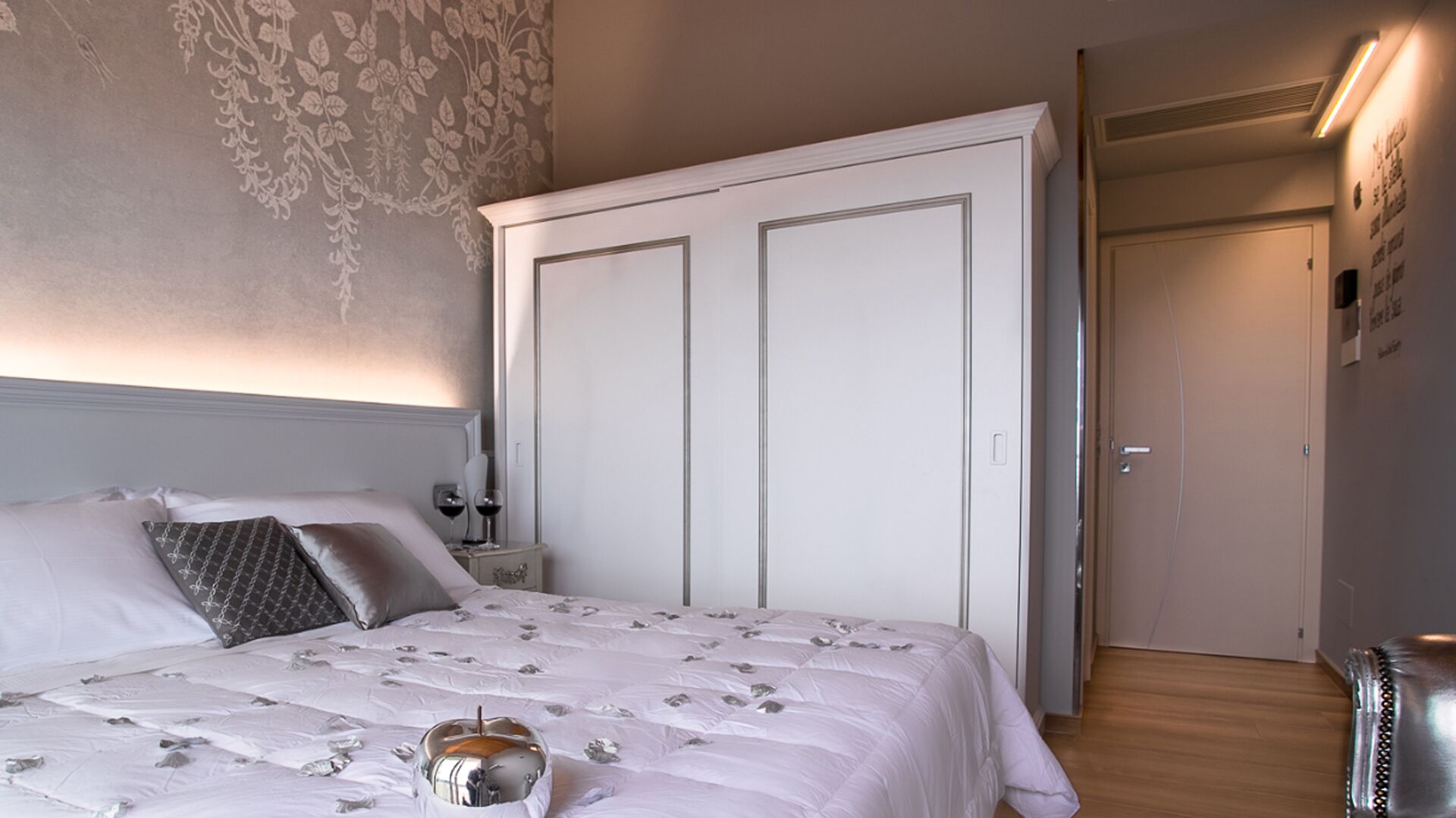 Un dormitorio con una cama grande, un armario, una mesita de noche con lámpara y un espejo.