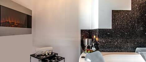 A modern hotel room with a fireplace, a small table with candles, and a decorative wall with mosaic tiles.