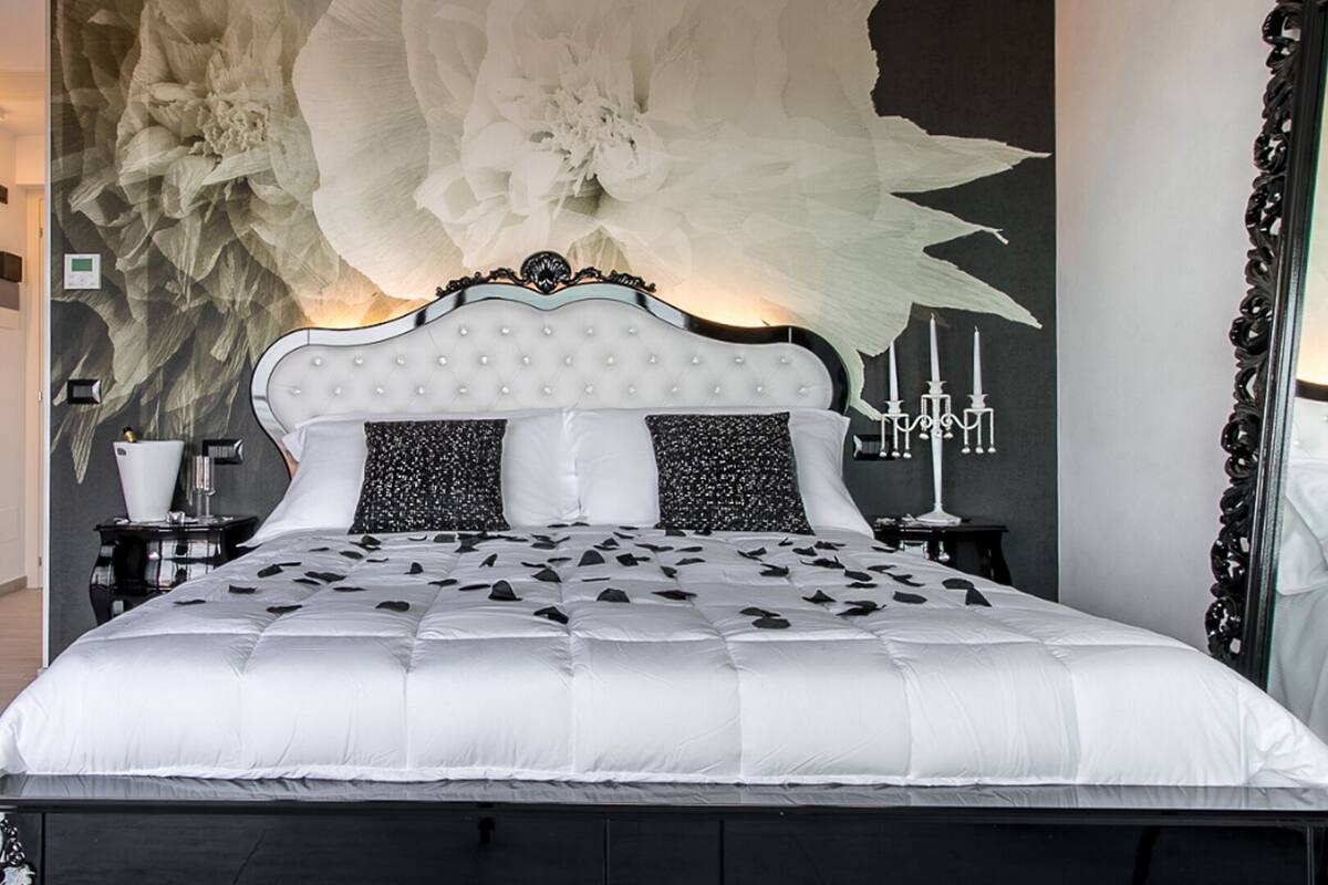 A bedroom with a large bed, a decorative wall with a floral pattern, and a mirror with an ornate frame.