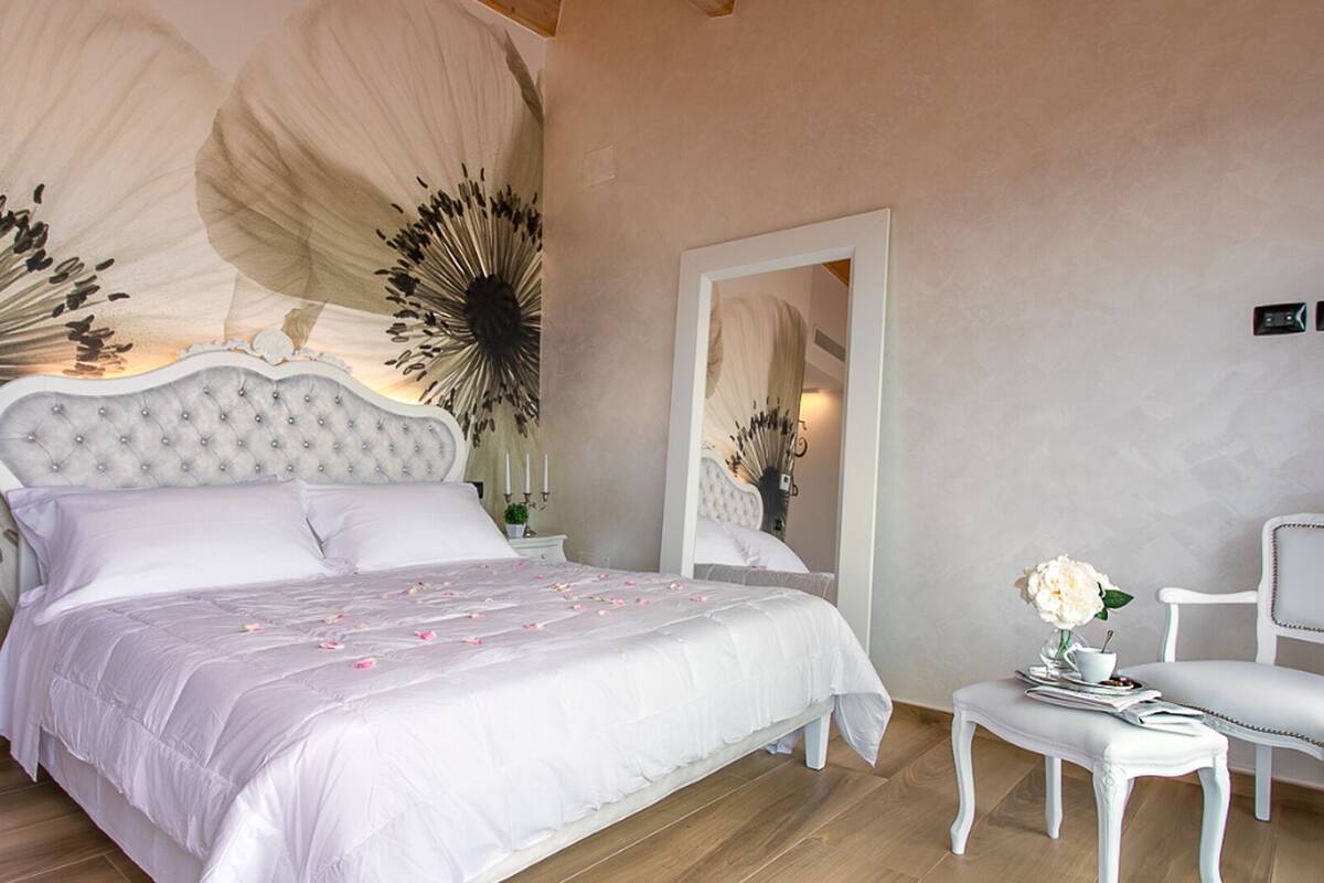 A bedroom with a large bed, a nightstand, a chair, and a mirror.