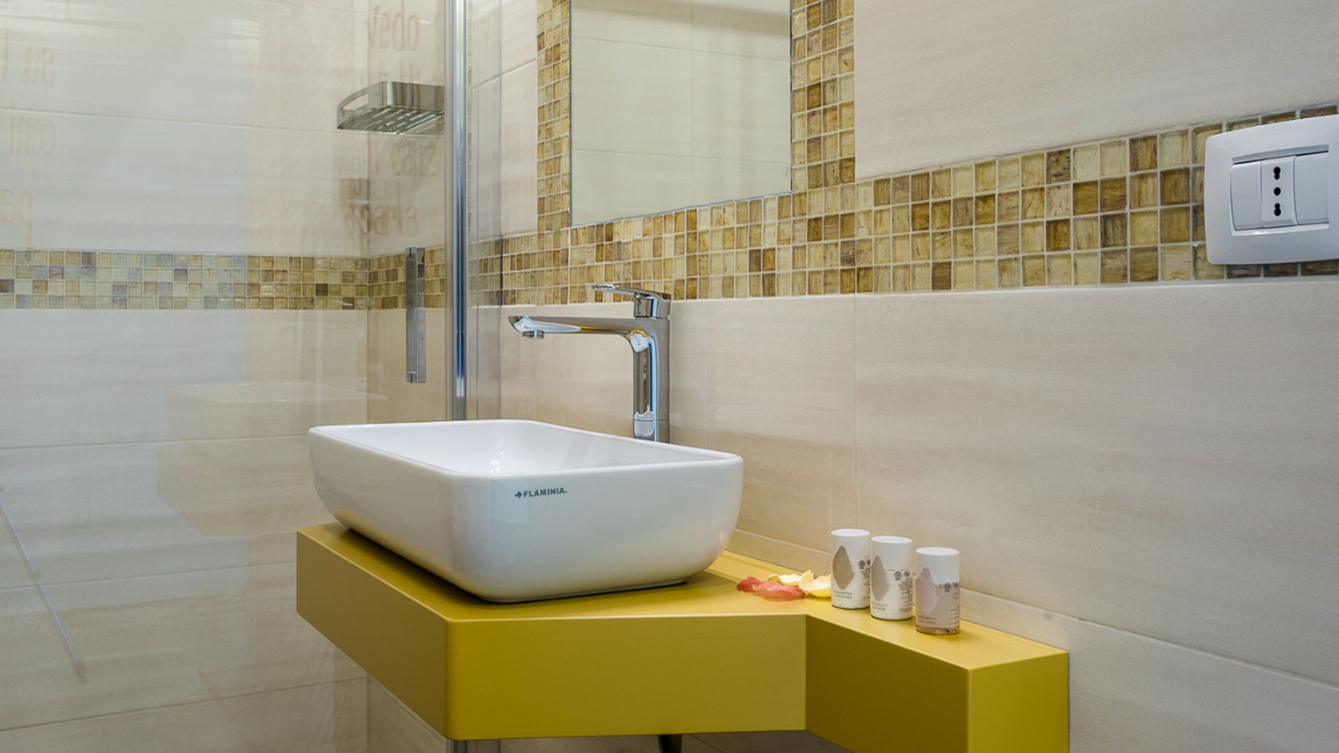 A bathroom with a white vessel sink, yellow vanity, and a glass shower enclosure.