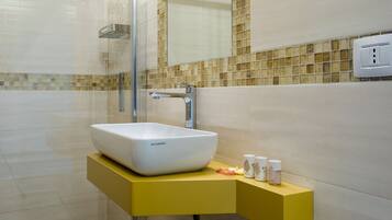A bathroom with a white vessel sink, yellow vanity, and a glass shower enclosure.